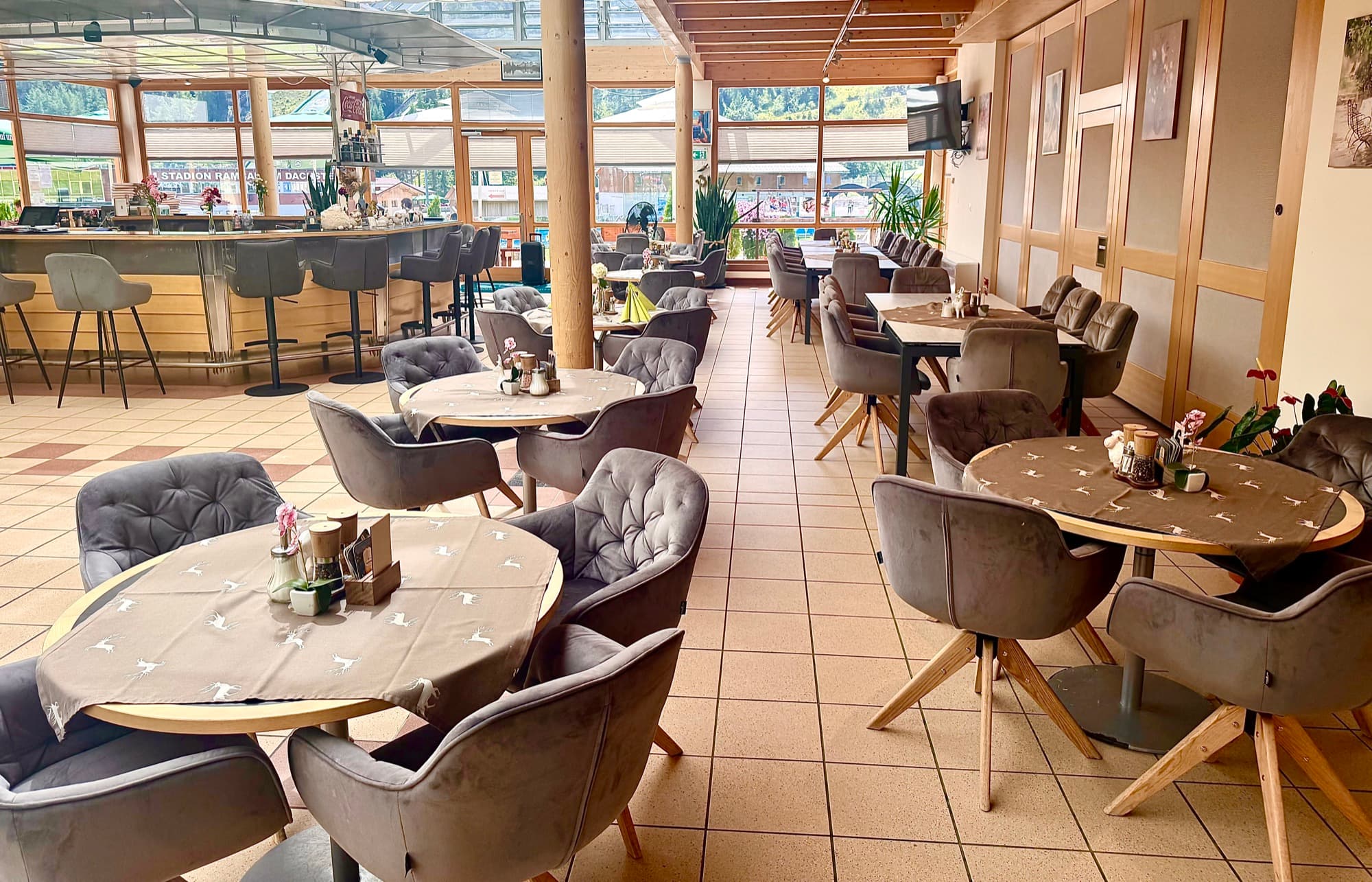 Bright dining room of Zentrum Café Restaurant with plush grey armchairs, round wooden tables and the bar beneath timber beams